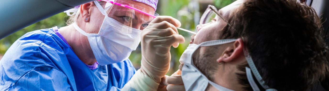 Nurse leaning into a car taking a Covid 19 swab from a man