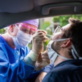 Nurse leaning into a car taking a Covid 19 swab from a man