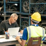 A manager sitting at a desk interviewing an employee wearing PPE equipment