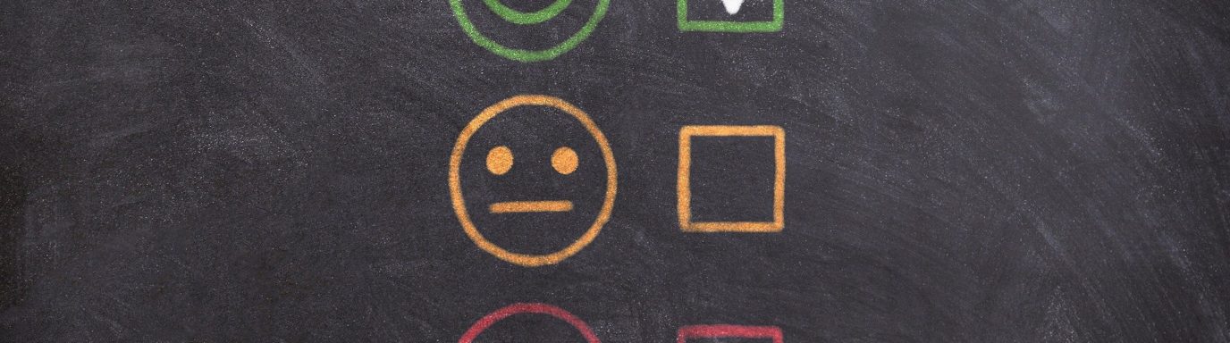 A blackboard with smiley face rating system - sad face to happy face