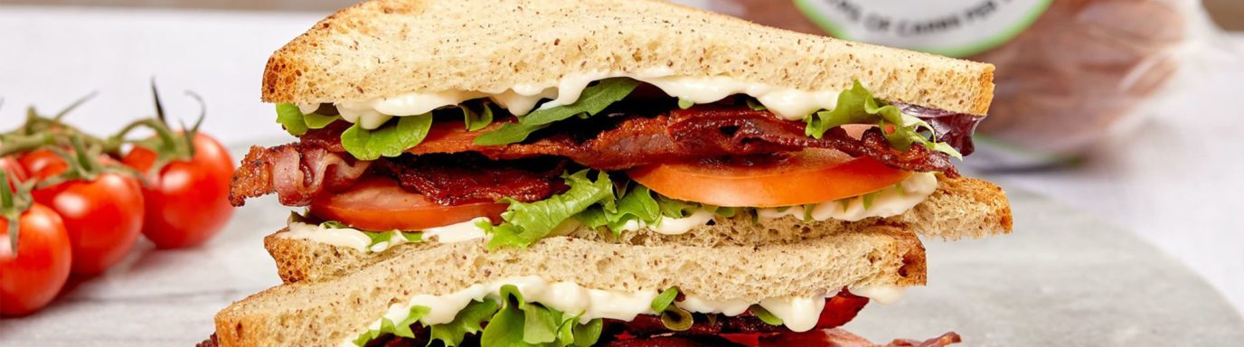 A double-stacked sandwich on a plate containing bacon, lettuce and tomato