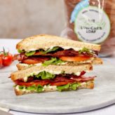 A double-stacked sandwich on a plate containing bacon, lettuce and tomato