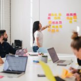 A female employee presenting to her team during a meeting using colourful post-it notes stuck to the wall
