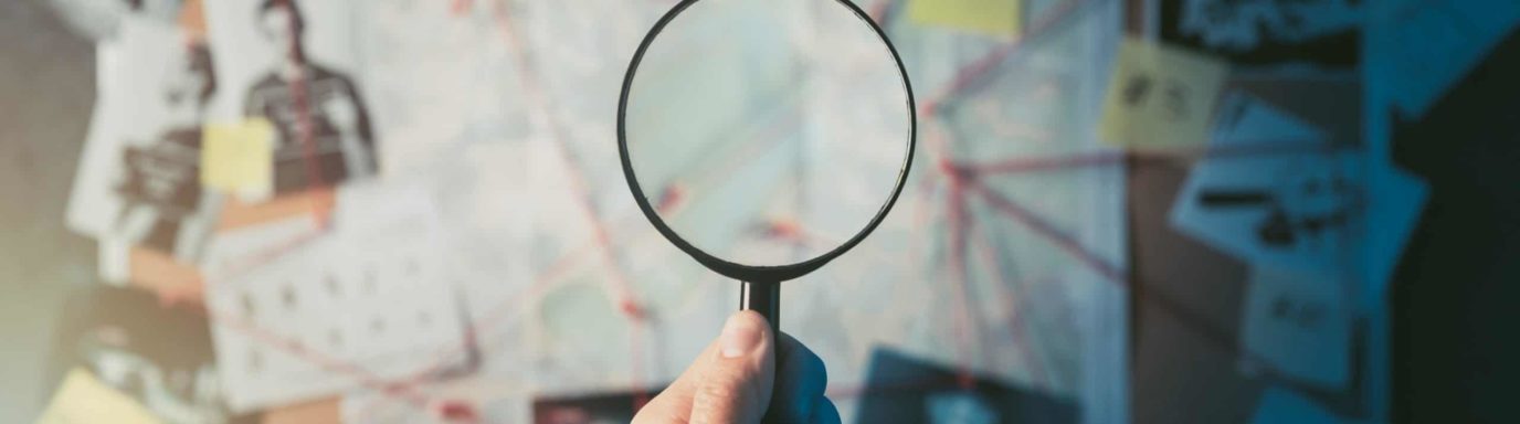 A Magnifying glass being held over a pile of investigation paperwork