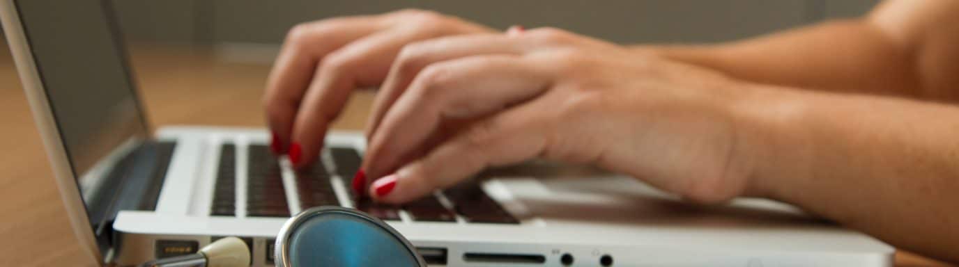 A female doctor typing on a laptop with stethescope in foreground