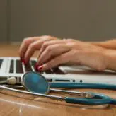 A female doctor typing on a laptop with stethescope in foreground
