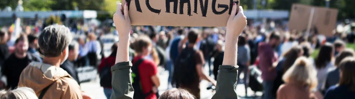 Person holding up a sign that reads 'we need a change'