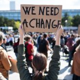 Person holding up a sign that reads 'we need a change'