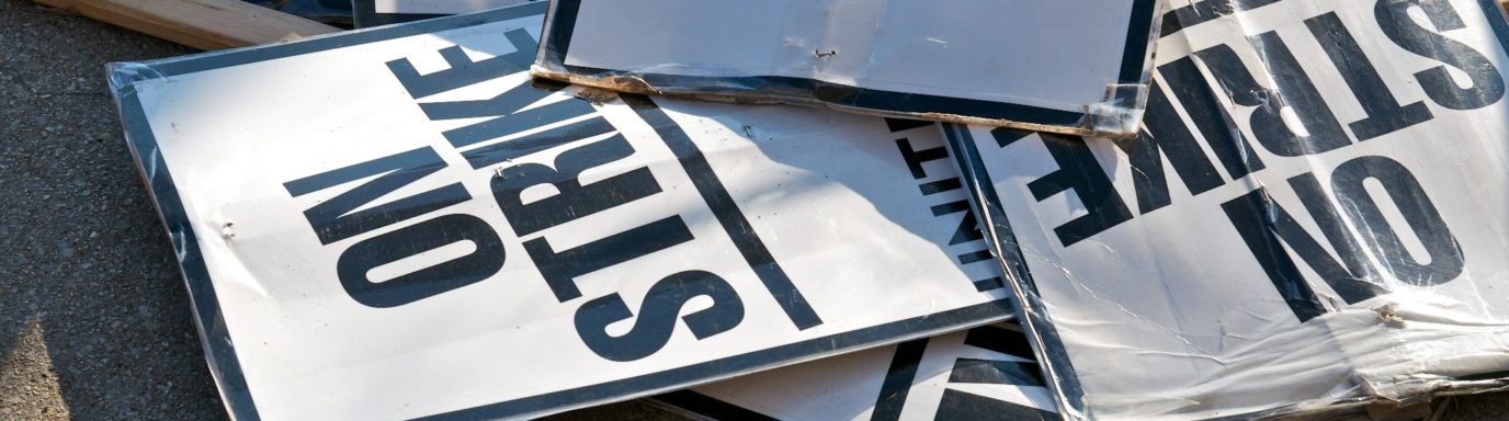 A pile of signs on the floor that say 'on strike'